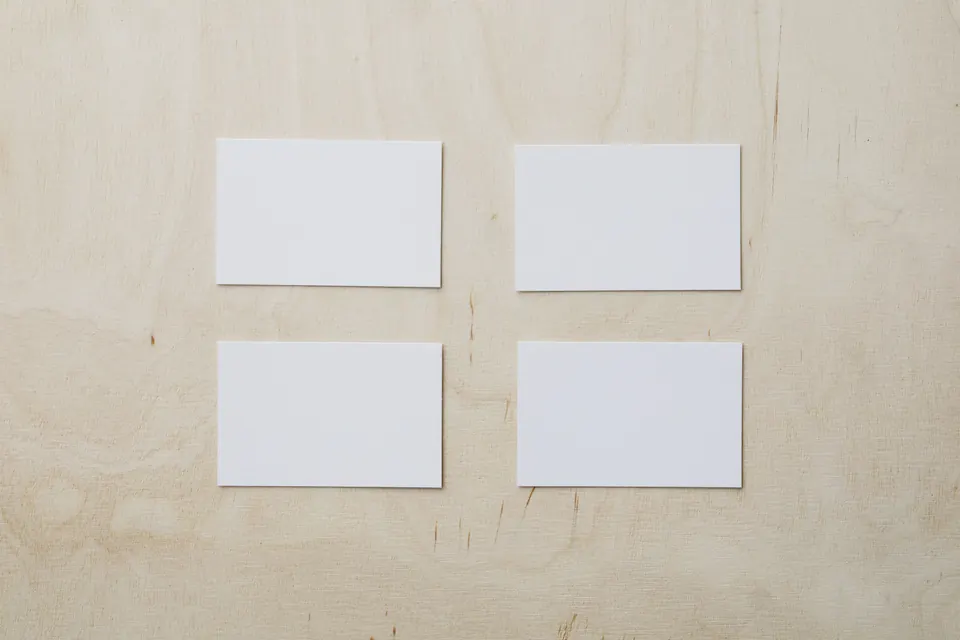 Quatre cartes rectangulaires blanches et vierges, en deux rangées sur un plan de contreplaqué de bouleau clair, vues de dessus