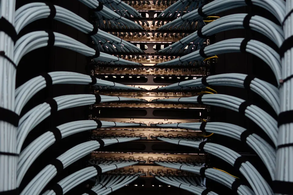 Symmetrical bundles of pale blue network cables with black ties, curving toward a lit patch panel in a dark server rack