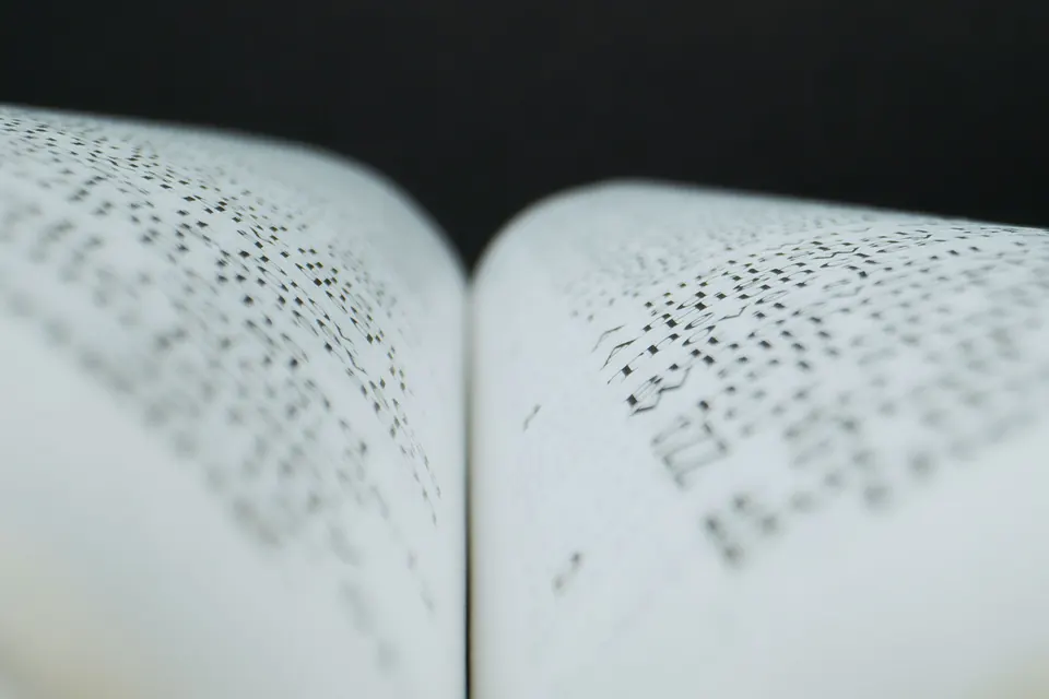 Makroaufnahme eines aufgeschlagenen Buches mit kleinen, dicht gesetzten Schriftzeichen, unscharf und unlesbar, vor Schwarz